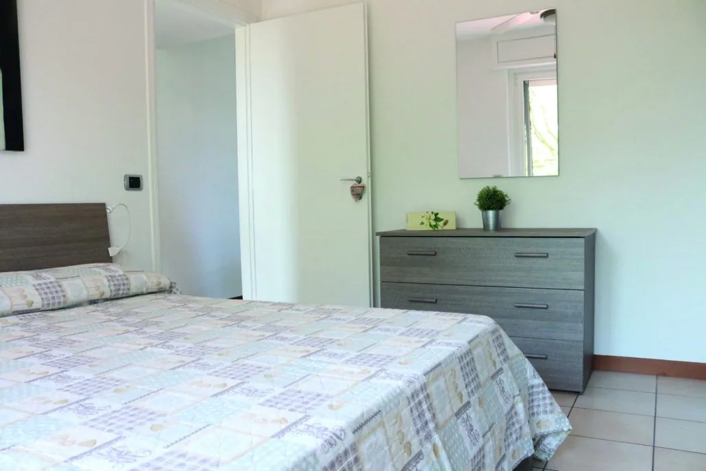 Camera matrimoniale di Casa Martina con letto vestito in tonalità chiare, comò grigio e specchio