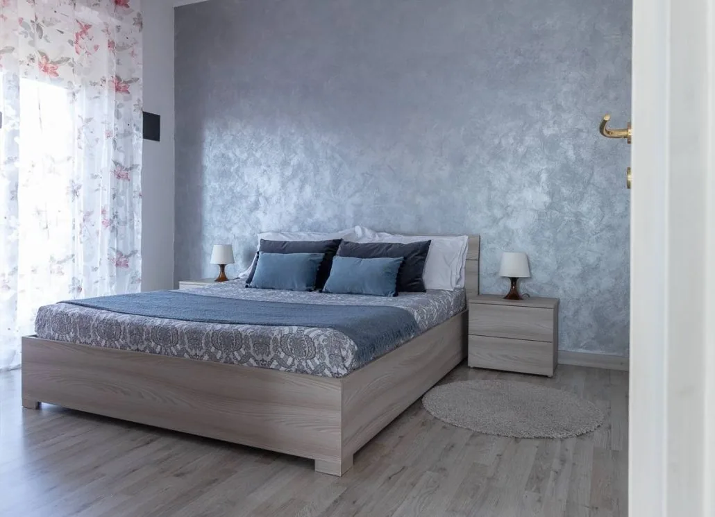 Camera matrimoniale de Il Girasole con parete decorativa azzurra, letto in legno chiaro e comodini con abat-jour