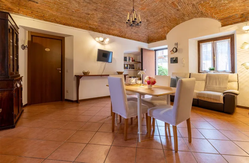 Wohnzimmer von Il Monastero mit offenem Ziegelgewölbe, Eisenleuchter, weißem Esstisch und Terrakottaboden